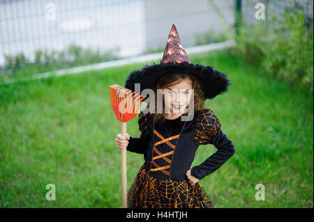 Preparazione per la festa di Halloween. La ragazza in un abito della strega malvagia pulisce un prato di rastrello. La ragazza è vestita di un nero-arancio di dre Foto Stock