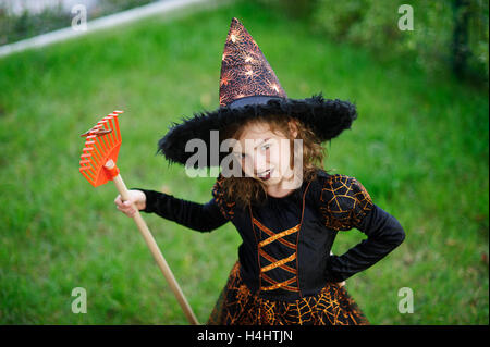 Preparazione per la festa di Halloween. La ragazza in un abito della strega malvagia pulisce un prato di rastrello. La ragazza è vestita di un nero-arancio di dre Foto Stock