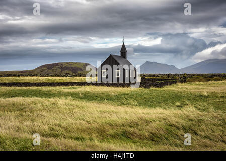 Scenario di legno nero chiesa di Budir in Islanda con il pascolo e le montagne sullo sfondo Foto Stock