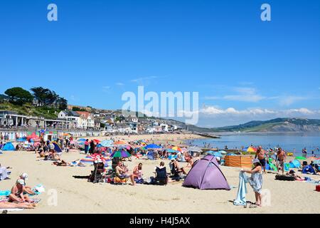 I villeggianti rilassante sulla spiaggia sabbiosa con il lungomare e la spiaggia di capanne per la parte posteriore, Lyme Regis, Dorset, Inghilterra, Regno Unito. Foto Stock