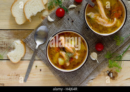 Zuppa di pomodoro con salmone in un vaso di ceramica, pane e pomodori su assi di legno dello sfondo. Foto Stock