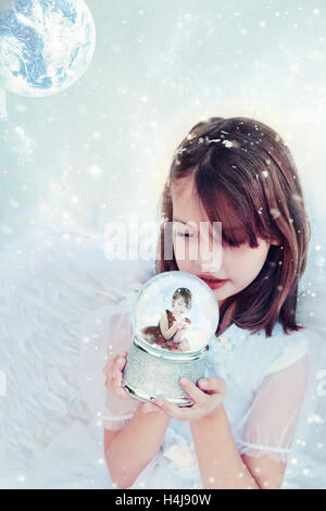 Little Angel detiene un snow globe orologi e una bambina all'interno lavori di soffiaggio della neve. Foto Stock