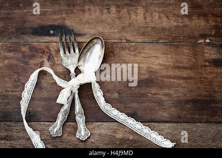 Argenteria antica cucchiaio e forchetta legate con nastro in pizzo su un vecchio rustico sfondo di legno con un grunge come si sentono. Foto Stock