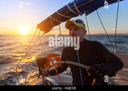 Capitano sterza il yacht a vela sul mare durante il tramonto. Foto Stock