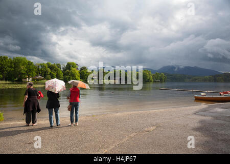 Vista posteriore di tre donne e due di essi il ricovero sotto un ombrello. Staffelsee. Alta Baviera. Germania. Foto Stock