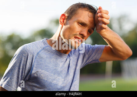 Stanco di esercizio e di calore uomo sportivo tergi sudore dal viso Foto Stock