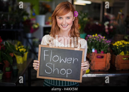 Ritratto di donna fioraio azienda ardesia con negozio di fiori segno Foto Stock