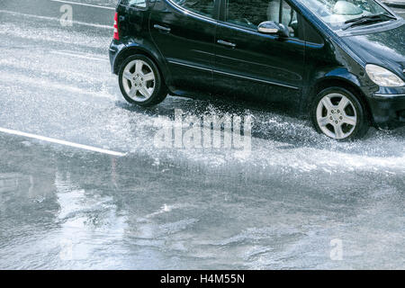 Guida auto sulla strada allagata dopo la pioggia con spruzzi di acqua dalle ruote per auto Foto Stock