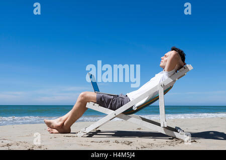 Imprenditore di successo in appoggio su una spiaggia tropicale con il computer portatile Foto Stock