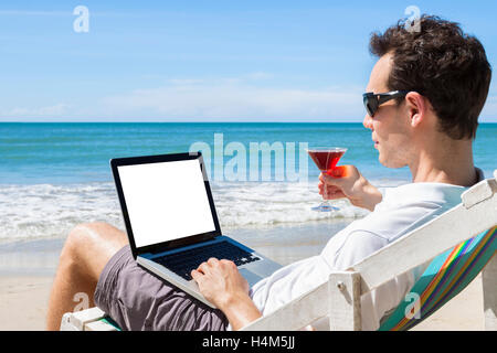 Freelance indipendente la scrittura di messaggi di posta elettronica sulla spiaggia tropicale con un cocktail in mano Foto Stock