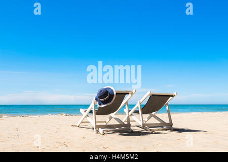 Bianco di due sdraio e un cappello per rilassarsi sulla spiaggia, luminosa giornata di sole Foto Stock