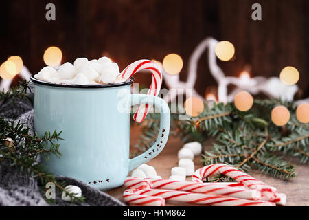 Smalto tazza di cioccolata calda con mini marshmallows e candy canes con rami di pino e sciarpa grigio contro un sfondo rustico con Foto Stock