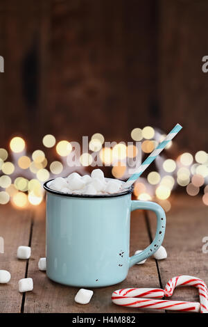 Smalto tazza di cioccolata calda con mini marshmallows e candy canne in forma di cuore contro un sfondo rustico. Foto Stock