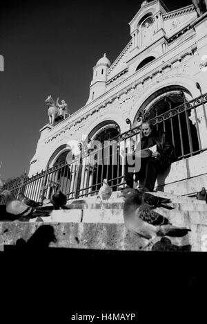 Uomo che legge il giornale sui gradini della chiesa del Sacré Coeur, Montmatre, Parigi Foto Stock