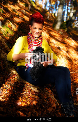 Carina ragazza con cane nero sorridente e abbracciando presso la foresta di autunno all'esterno. Foto Stock