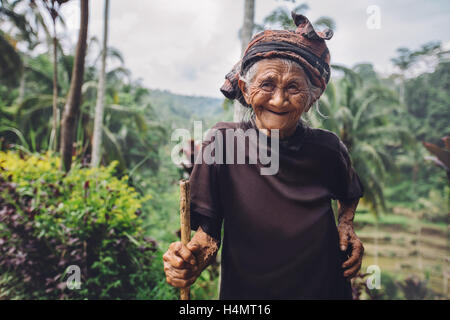 Ritratto di donna senior in piedi con un bastone e sorridente. Vecchia femmina con uno splendido sorriso sul suo viso all'aperto in campagna. Foto Stock