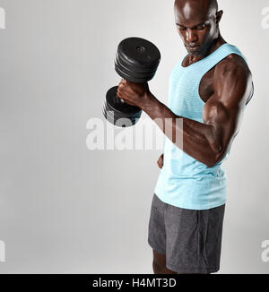 Montare il giovane africano esercizio con manubri contro uno sfondo grigio. Muscoloso maschio nero modello pesante di sollevamento pesi. Foto Stock