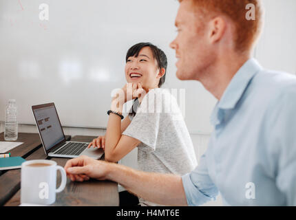 Due giovani felice la gente di affari seduti ad un tavolo per conferenza durante la riunione di affari. I colleghi seduti nella sala riunioni con il computer portatile Foto Stock