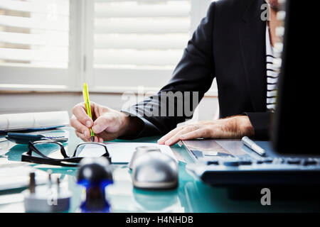 Un uomo seduto alla scrivania in ufficio, tenendo una penna. Foto Stock