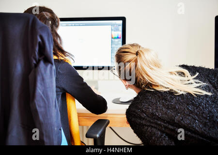 Due donne seduti condividere lo schermo di un computer e di discutere il contenuto grafico. Foto Stock