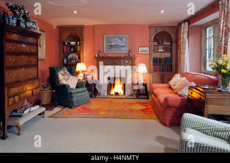 Un accogliente tradizionalmente salone arredato con mobili di antiquariato e uno scoppiettante fuoco aperto Foto Stock
