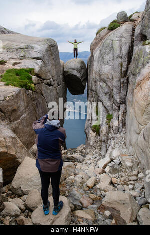 I turisti per scattare delle foto di amici su Kjeragbolten, una roccia appeso 1100 metri sopra il fiordo Lysefjorden, Norvegia Foto Stock