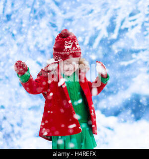 Bambina in giacca rossa e verde abito di maglia la cattura di fiocchi di neve in inverno park alla vigilia di Natale. Bambini a giocare all'aperto nella neve Foto Stock