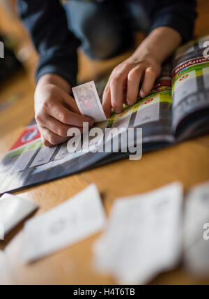 Un bambino di 8 anni del ragazzo è incollare il calcio carte commercio nella sua sticker collection scrapbook. Foto Stock