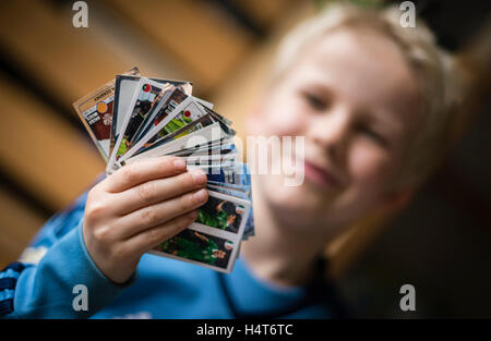 Un bambino di 8 anni è il ragazzo che mostra il suo calcio Panini scambio di carte prima di incollare nella sua sticker collection scrapbook. Foto Stock