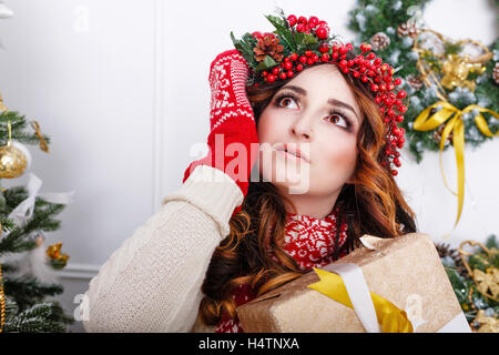 Bella ragazza in una sciarpa e guanti tenendo un dono sull'albero di Natale sfondo. L'atmosfera di festa. Foto Stock