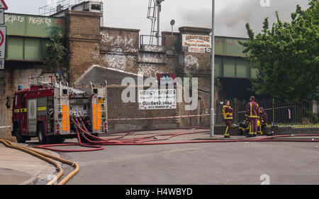Vigili del fuoco di Londra in stand by mentre le loro forniture di pompa acqua ad una pompa 10 il fuoco in un scrapyard. Foto Stock