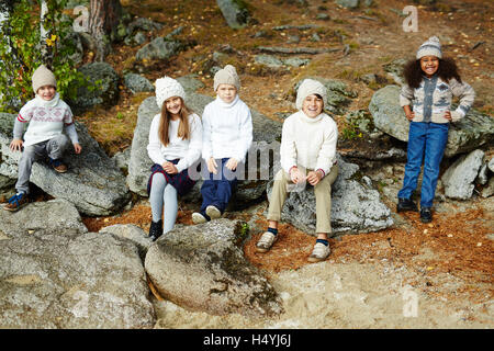 Carino kids in elegante-casual wear seduto su pietre in ambiente naturale Foto Stock