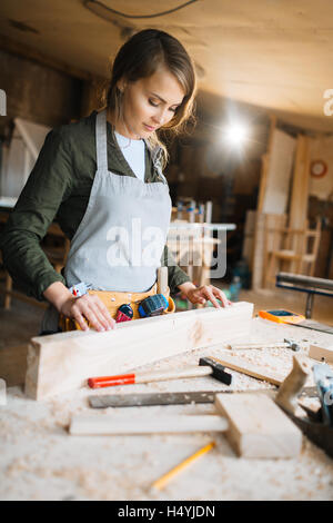 Giovane donna in uniforme di carpenter guardando tavolato in legno Foto Stock