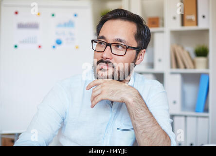 Giovane imprenditore in occhiali seduto in ufficio Foto Stock