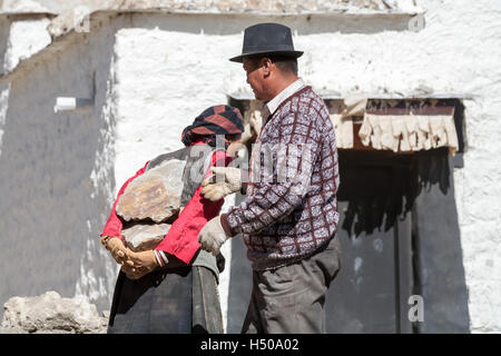 Un uomo tibetano rimuove una pietra pesante dalla schiena della donna tibetana. Old Lhatse, Tibet, Cina. Foto Stock