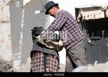 Un uomo tibetano rimuove una pietra pesante dalla schiena della donna tibetana. Old Lhatse, Tibet, Cina. Foto Stock