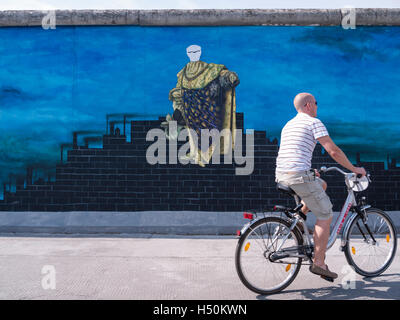 Uomo passato cicli di verniciatura di Erich Honecker sulla parete a East Side Gallery parte del vecchio Muro di Berlino a Berlino Germania Foto Stock