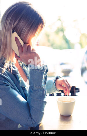 Giovane donna di bere caffé e parlando al telefono cellulare Foto Stock