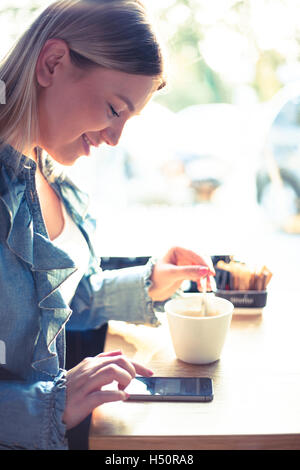 Giovane donna di bere il caffè e chattare su telefono cellulare Foto Stock