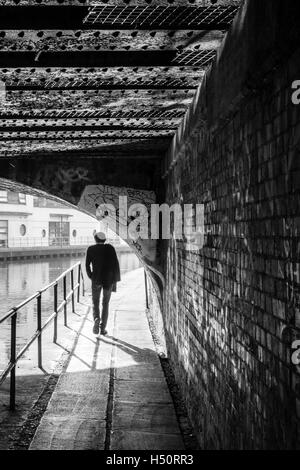 Immagine in bianco e nero di una singola persona camminando sotto un ponte sulla strada alzaia del Regent's Canal, stagliano e retroilluminato, London, Regno Unito Foto Stock