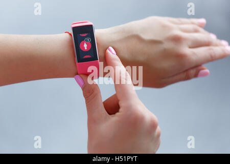 Femmina isolato mano con rosa smartwatch prendendo impulso dopo esercizio indoor su una luce e sfondo blured Foto Stock