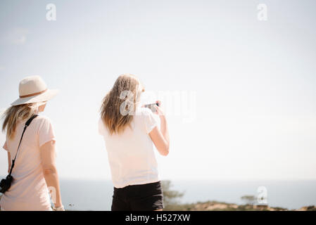 Donna e ragazza adolescente con lunghi capelli biondi all'aperto, tenendo in mano un telefono cellulare per scattare una foto. Foto Stock