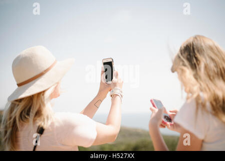 Donna e ragazza adolescente con lunghi capelli biondi all'aperto, tenendo in mano un telefono cellulare per scattare una foto. Foto Stock