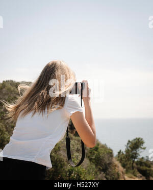 Ragazza con lunghi capelli biondi di guardare attraverso la fotocamera per scattare una foto. Foto Stock