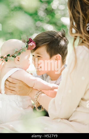 Una donna e un bambino e bambina con una ghirlanda di fiori sulla sua testa, seduto in un giardino. Foto Stock