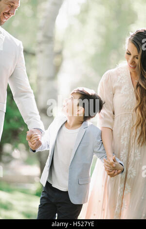 Padre, madre e figlio passeggiate all'aperto, tenendo le mani. Foto Stock