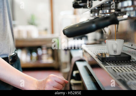 L uomo nella parte anteriore della macchina per il caffè espresso, espresso fresco in esecuzione in una coppa. Foto Stock