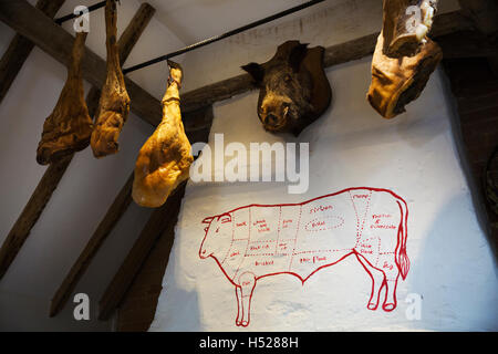 I prosciutti appesi al soffitto in una macelleria, un cinghiale farcito di testa sulla parete. Foto Stock