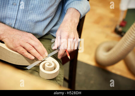 Un liutaio usando un righello per misurare il ricciolo di scorrimento della paletta di violino. Foto Stock