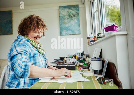 Una donna artista che lavora a una tavola utilizzando una grande blu pastello e il disegno su carta. Foto Stock